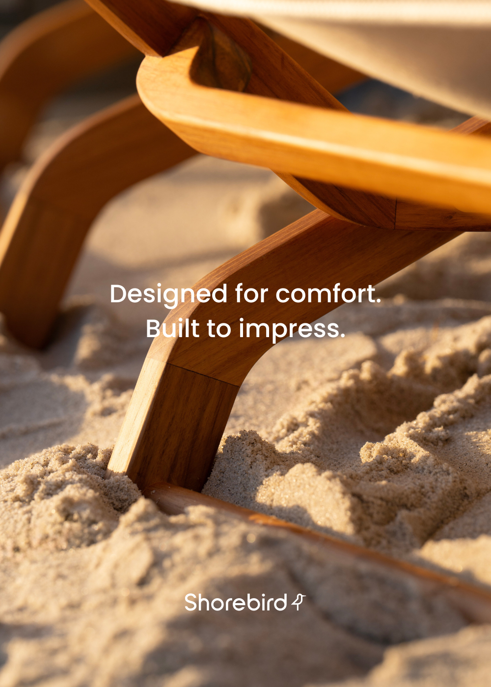 Close-up of Shorebird Chair leg in FSC-certified teak, resting in coastal sand at golden hour. Text overlay reads: “Designed for comfort. Built to impress.”