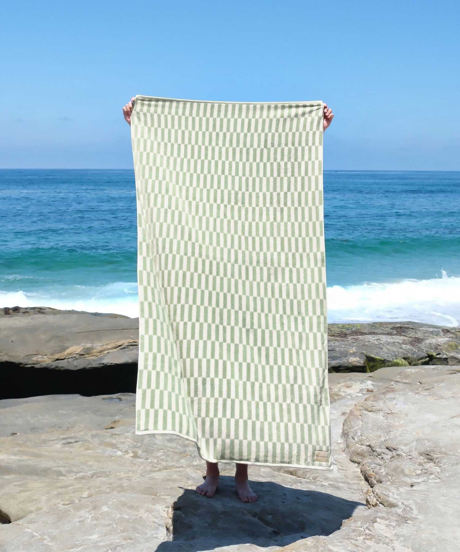 Person holding a striped oversized beach towel by the ocean