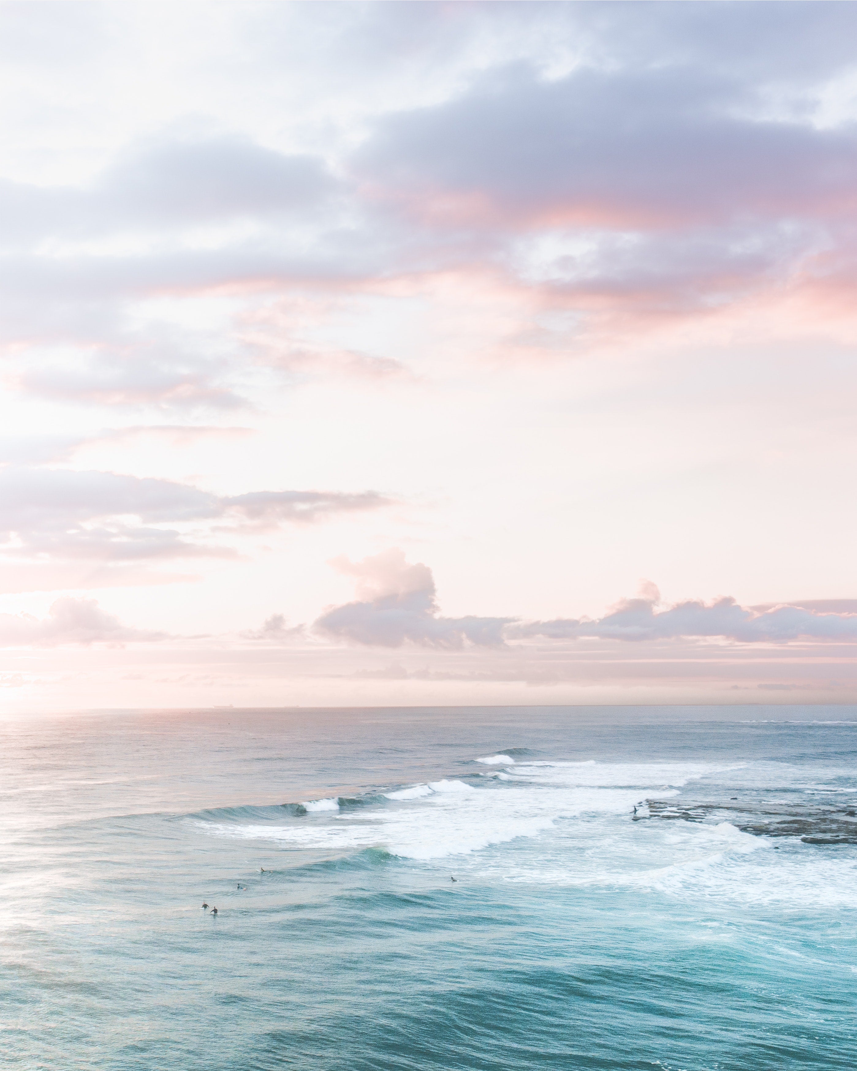 Aerial image of the ocean at sunrise with surfers