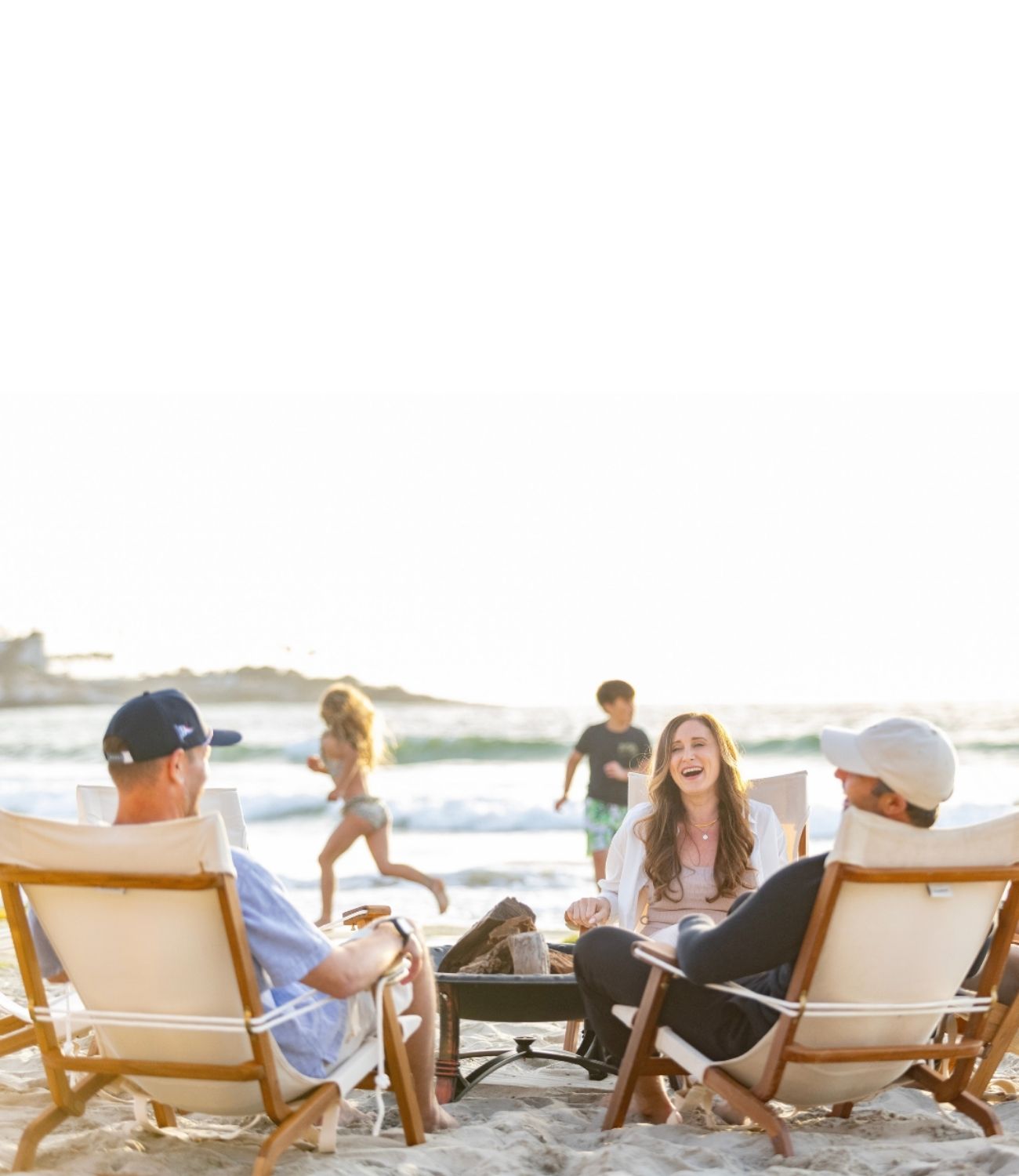 People sitting on Shorebird beach chairs by the water with children playing in the background