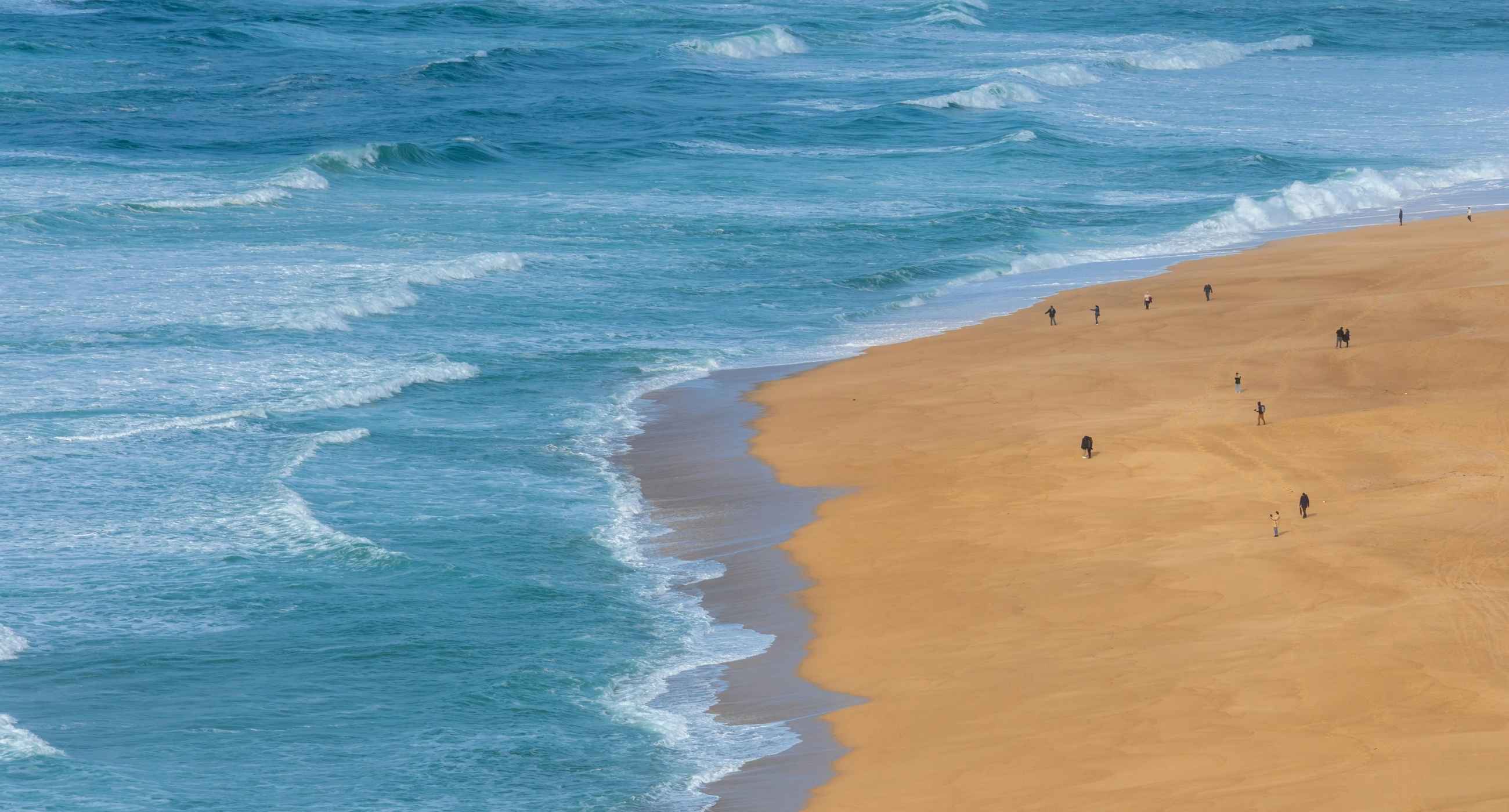ocean scene with people walking on sand.